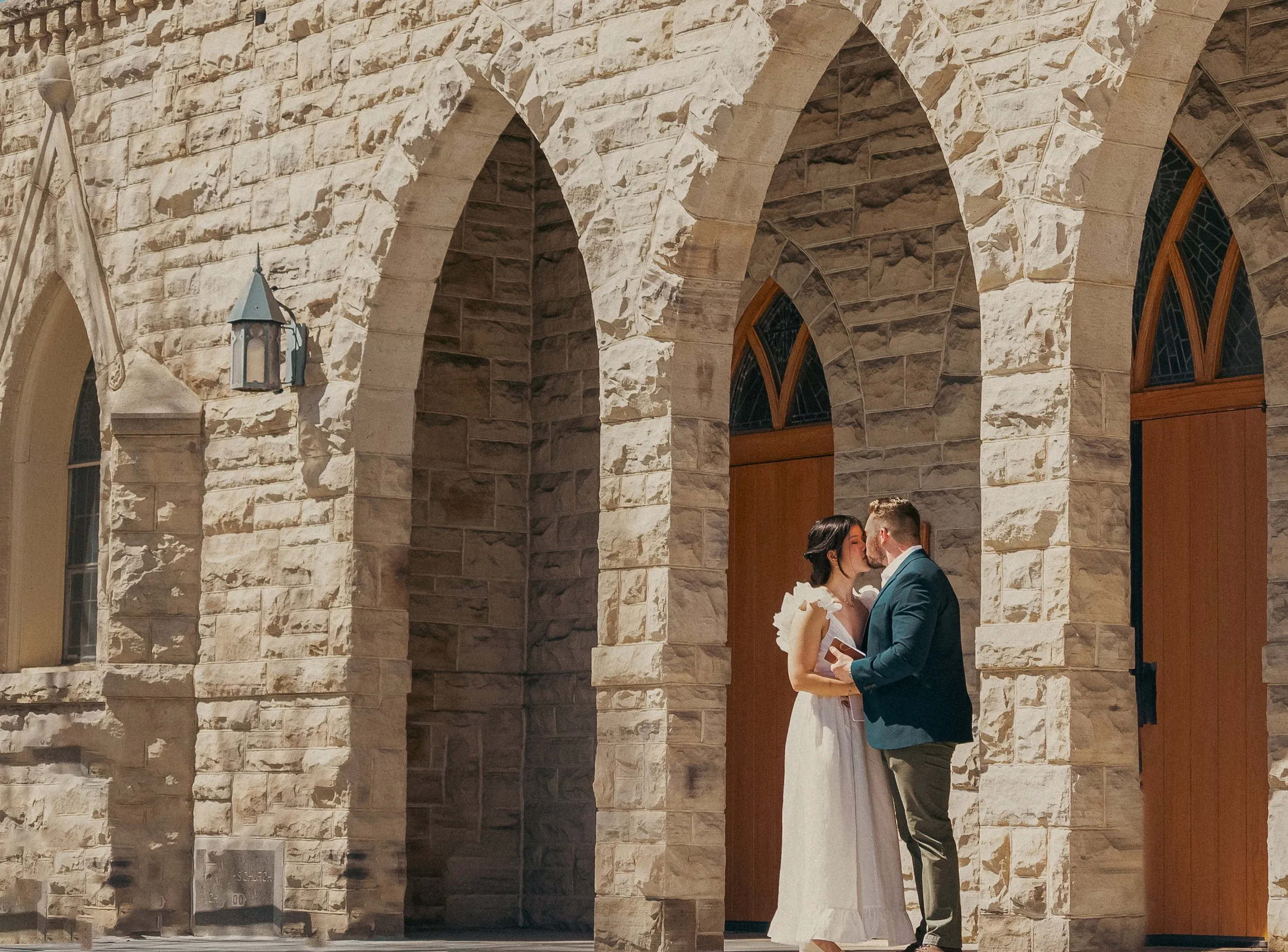 Couple kissing beneath stone chapel arches