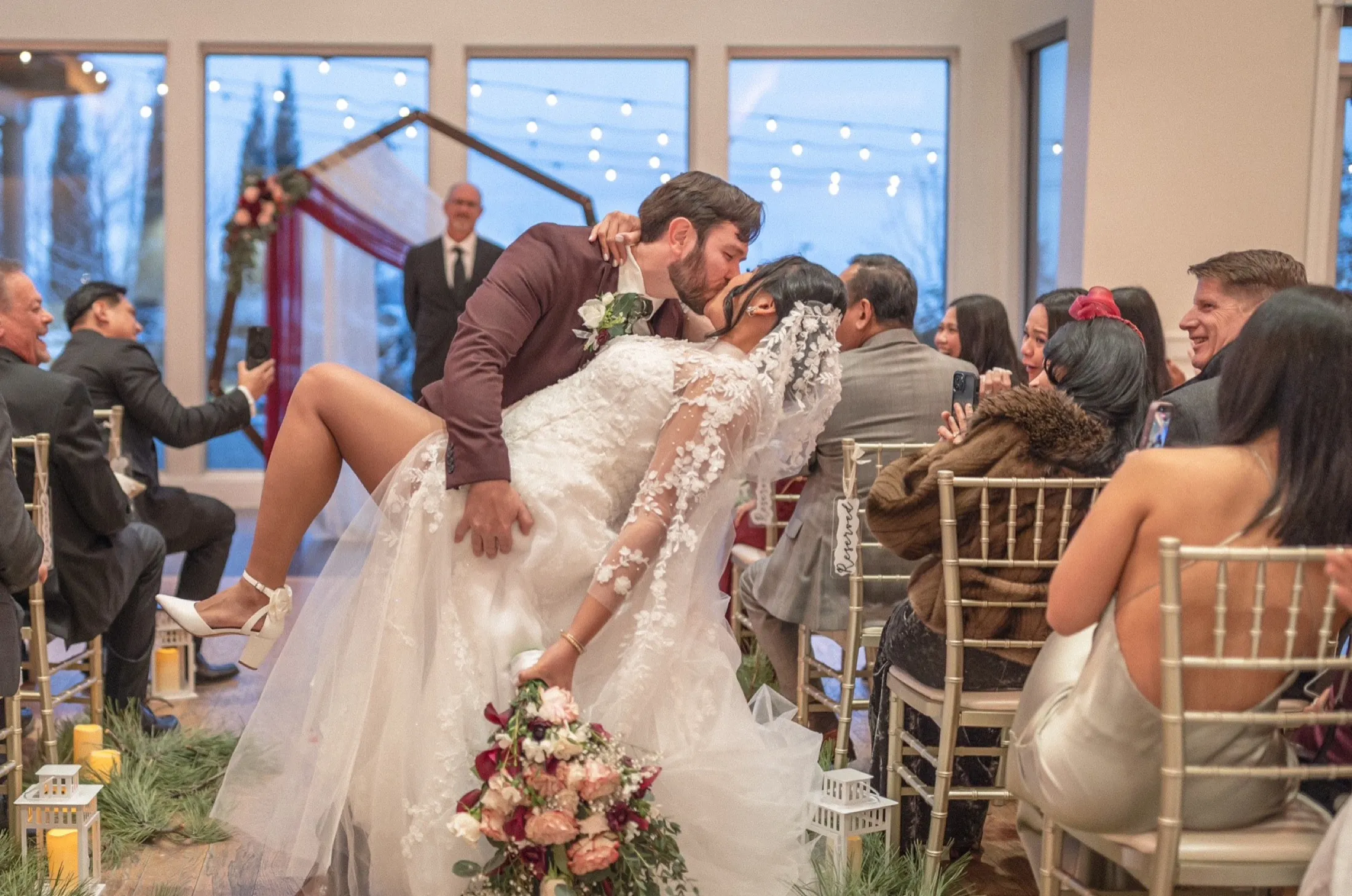 Groom dipping the bride for their first kiss as guests applaud from both sides of the aisle