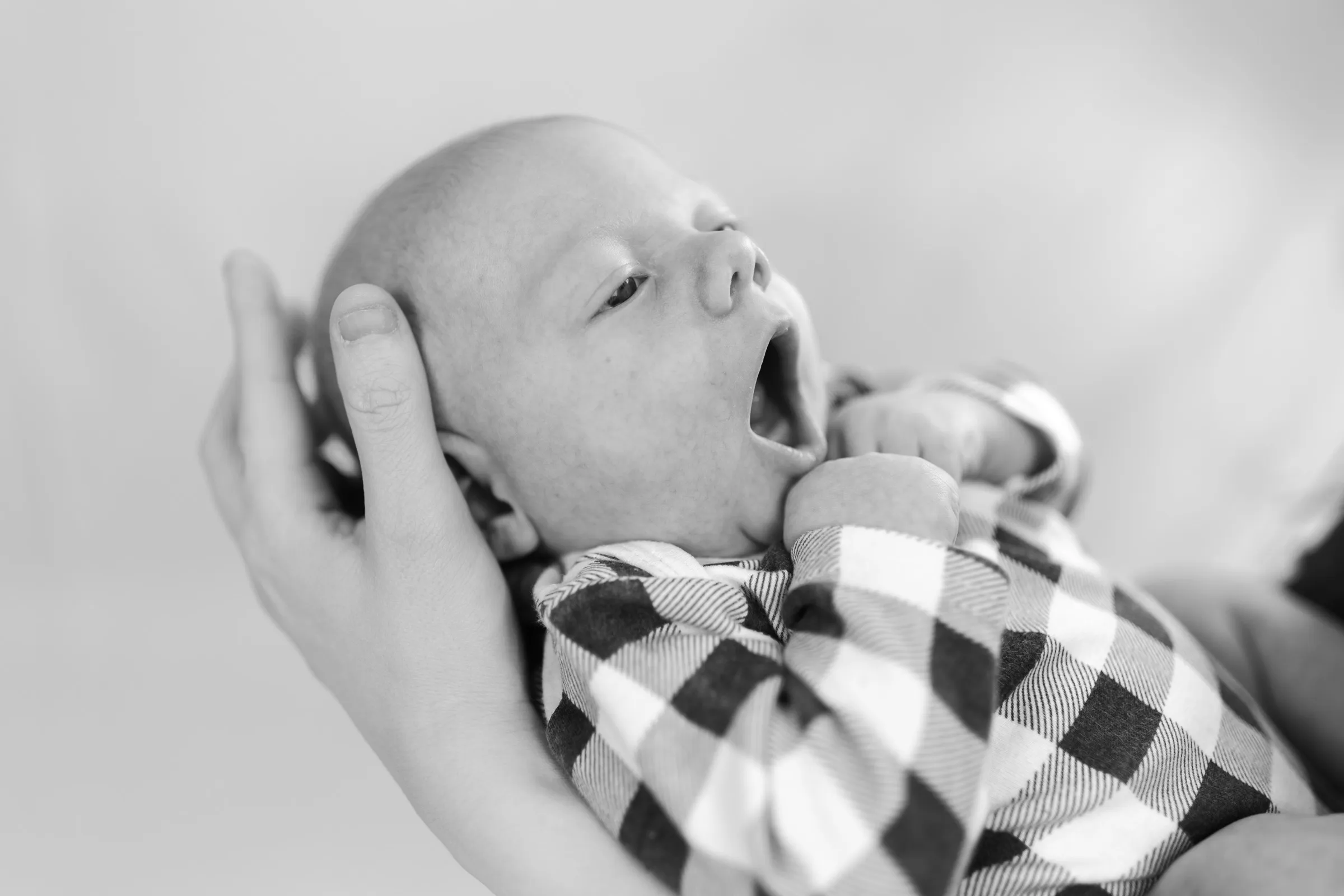 Newborn yawning in a parent’s hand