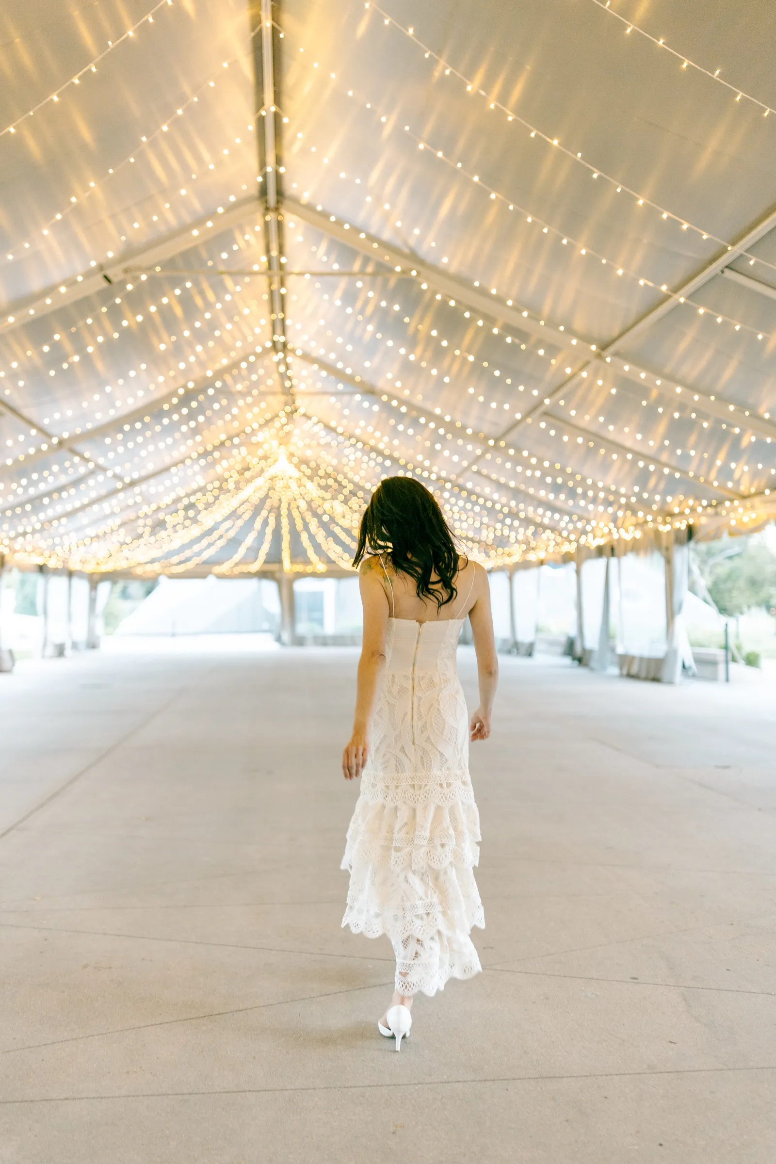 Bride walking beneath a tent ceiling strung with lights